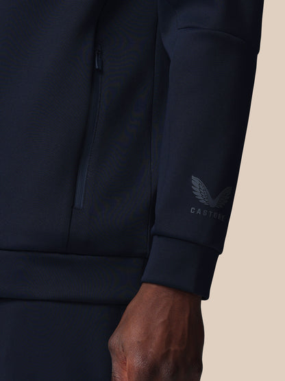 Navy blue jacket with a brand logo on the sleeve against a beige background