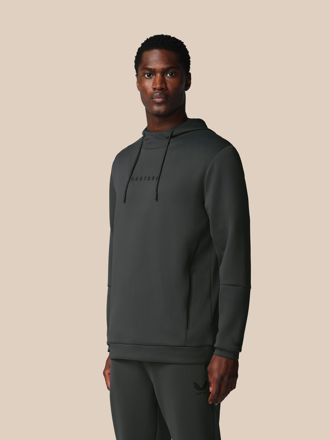 Man wearing a dark gray hoodie and pants on a beige background