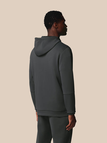 Person wearing a dark gray hoodie and pants on a beige background