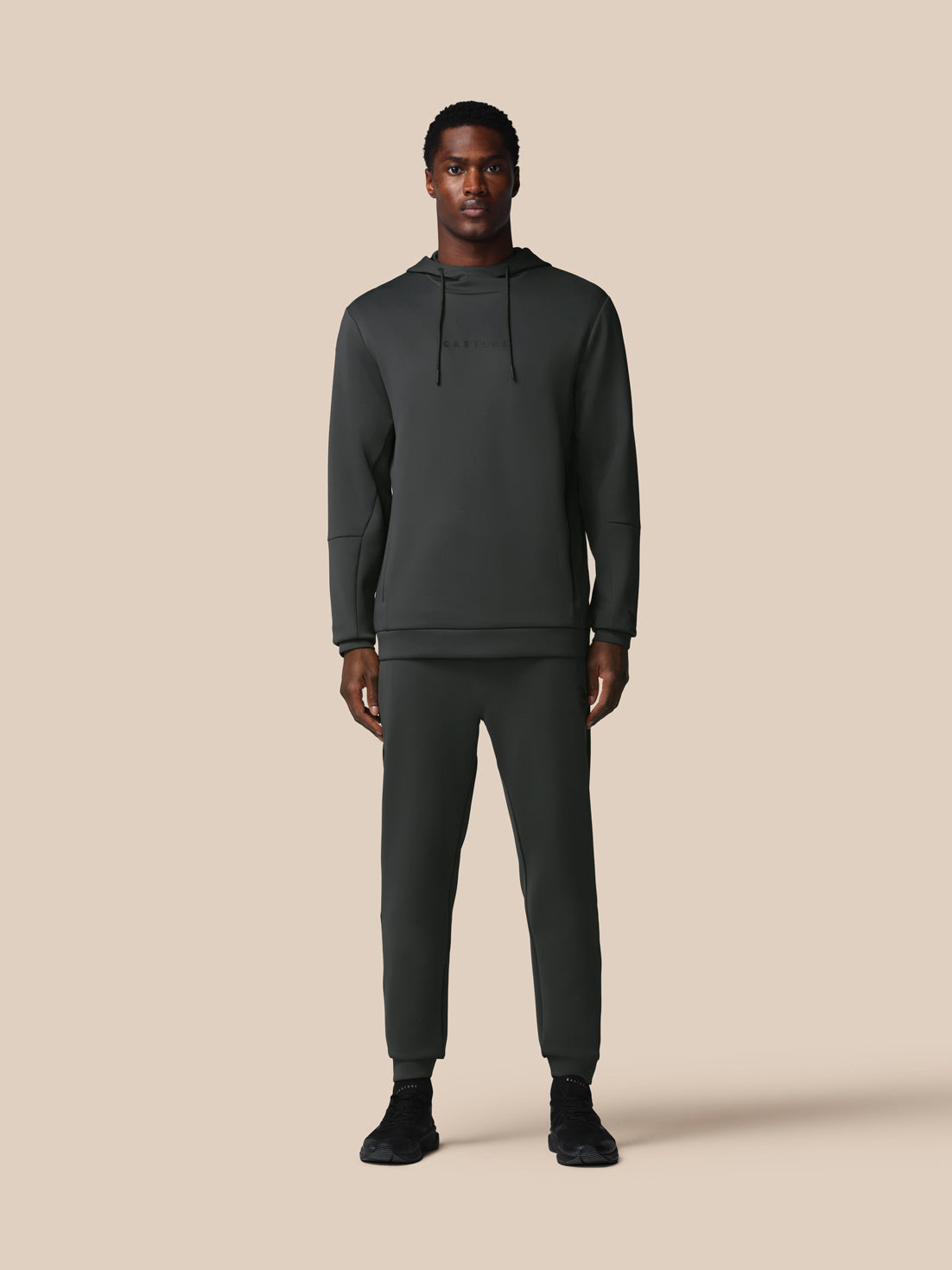 Man wearing a dark gray hoodie and pants on a beige background