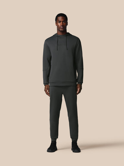 Man wearing a dark gray hoodie and pants on a beige background