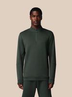 Man wearing a dark green long-sleeve shirt with a quarter zip on a beige background
