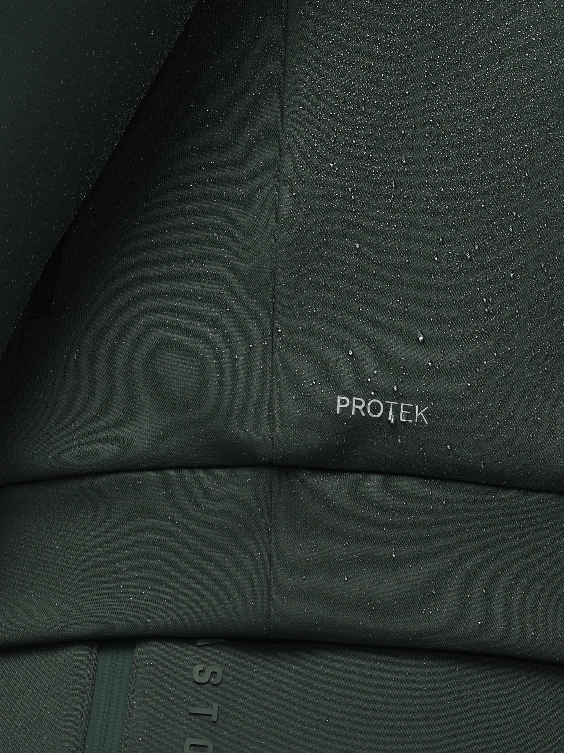 Close-up of a dark green fabric with 'PROTEK' branding, showing water droplets.