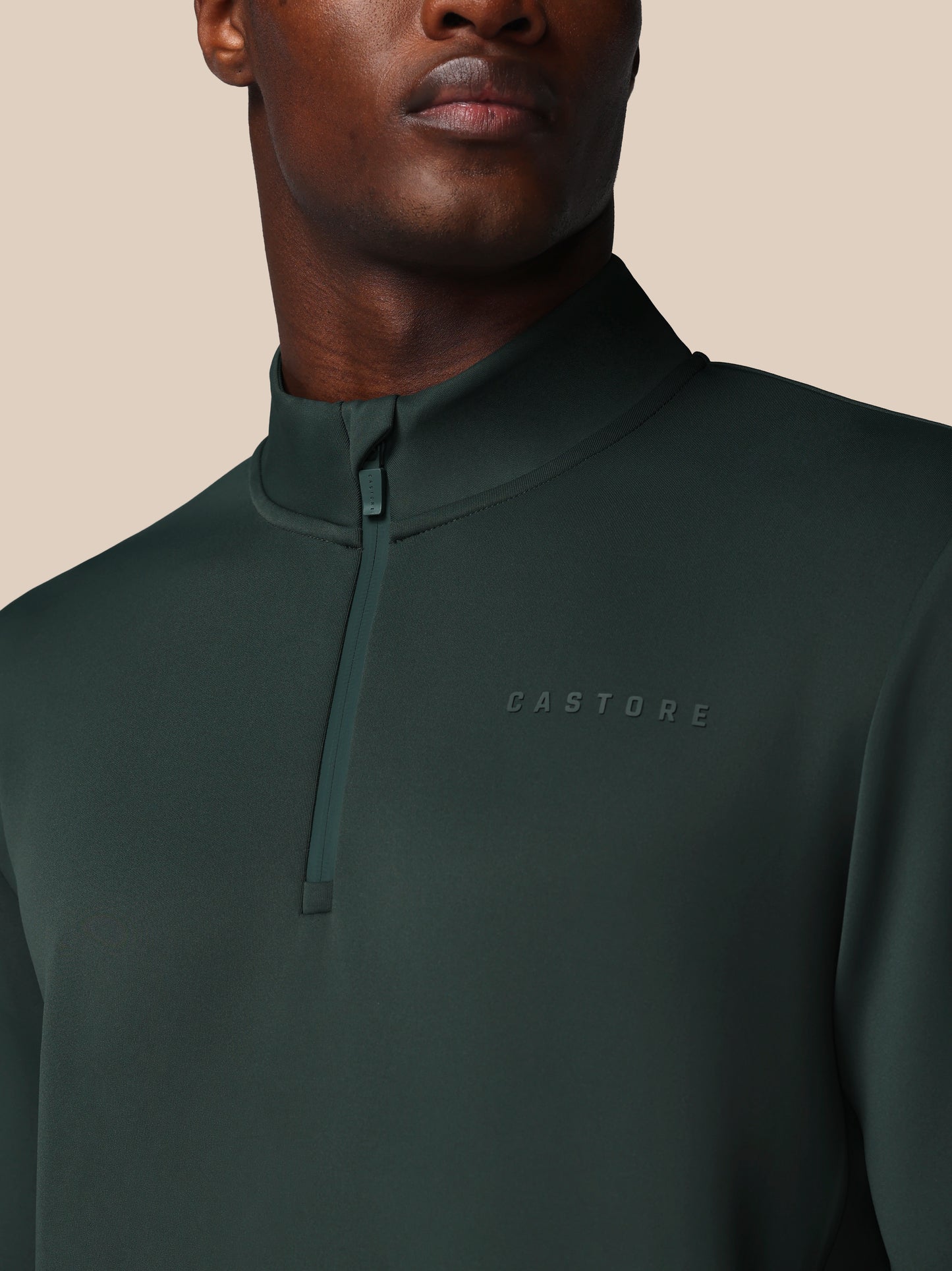 Man wearing a dark green quarter-zip pullover with 'CASTORE' branding on a beige background