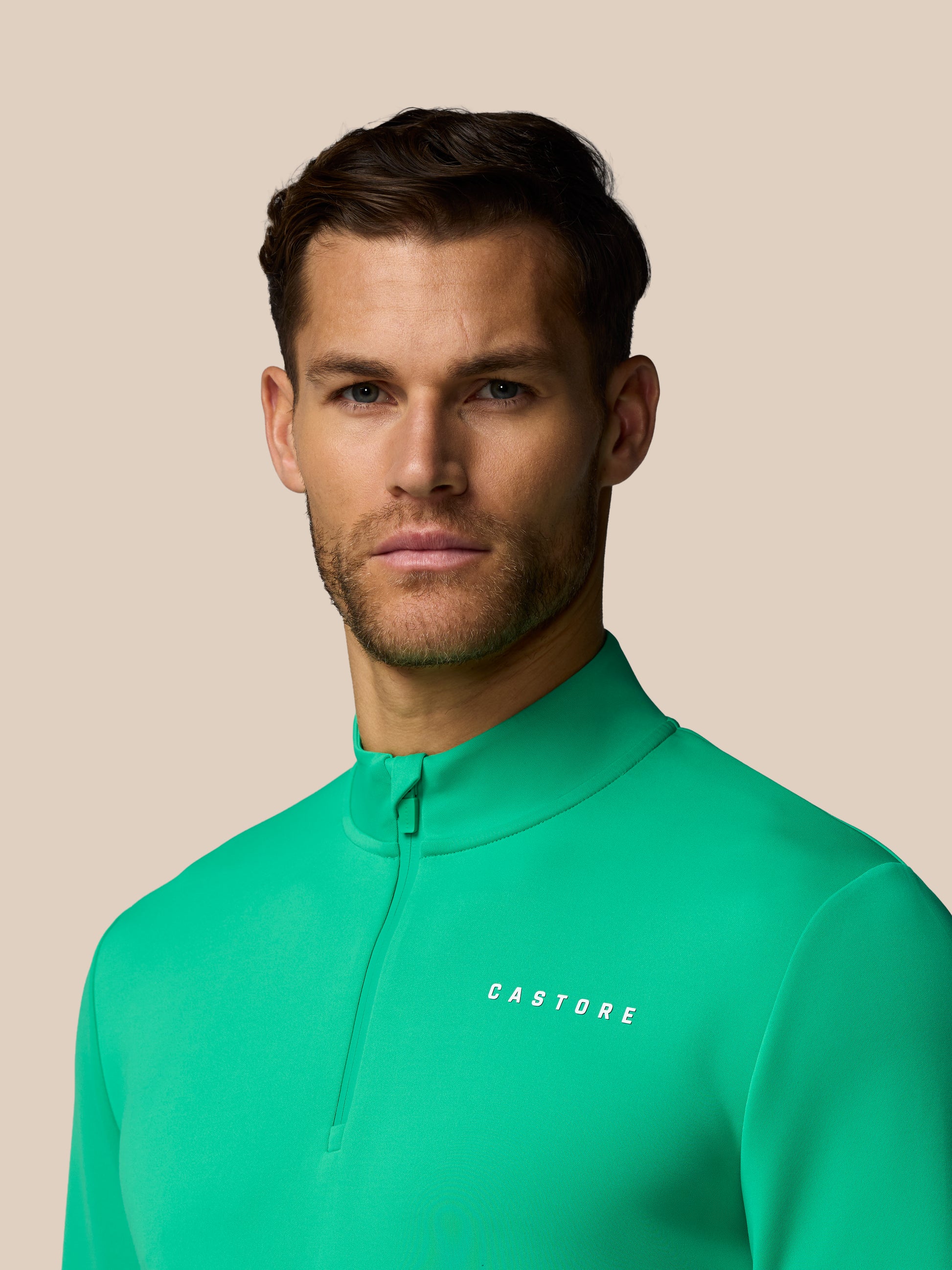 Man wearing a green cycling jersey with 'Castore' branding against a beige background