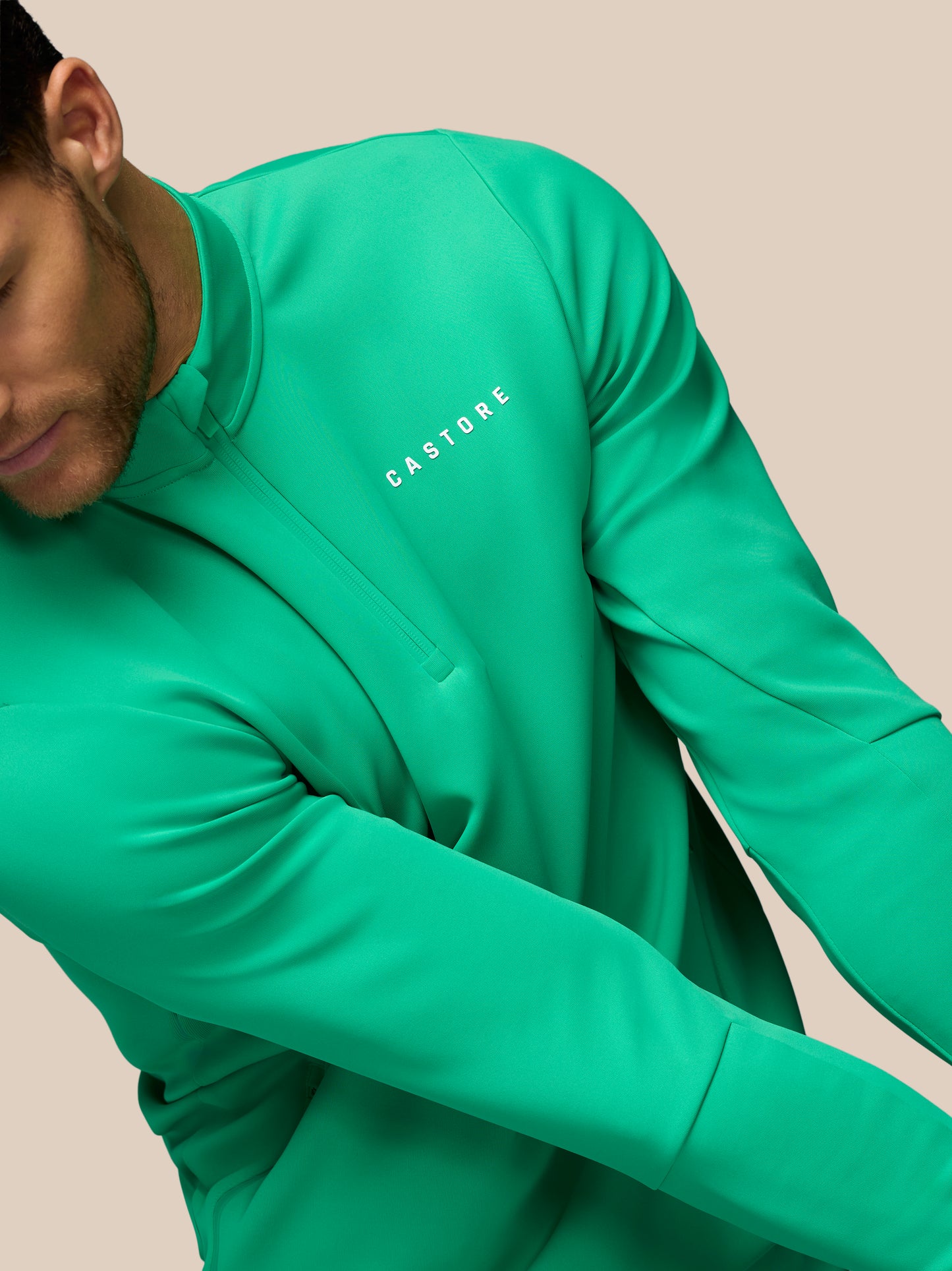 Person wearing a green long-sleeve shirt with 'Castore' branding on a beige background