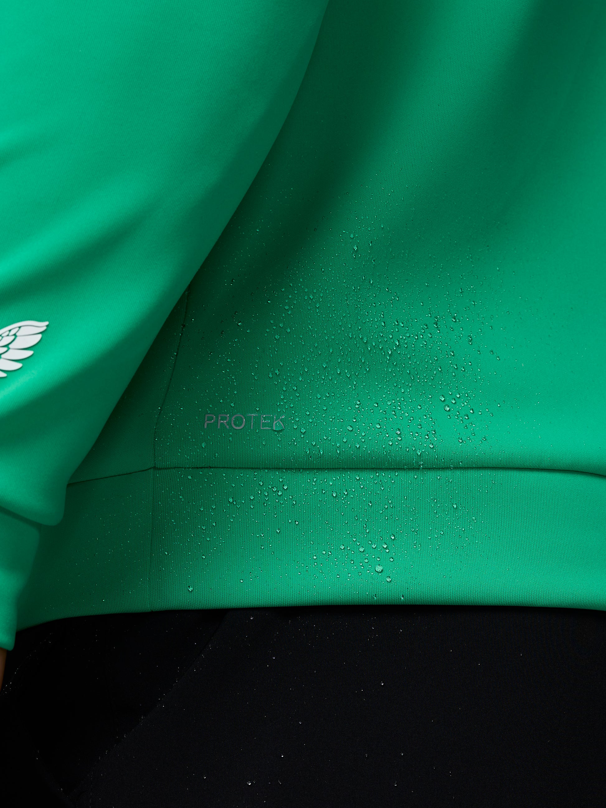 Close-up of a green jacket with water droplets on the fabric, featuring a brand logo.