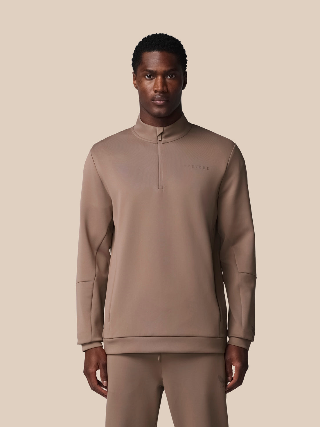 Man wearing a brown tracksuit against a beige background