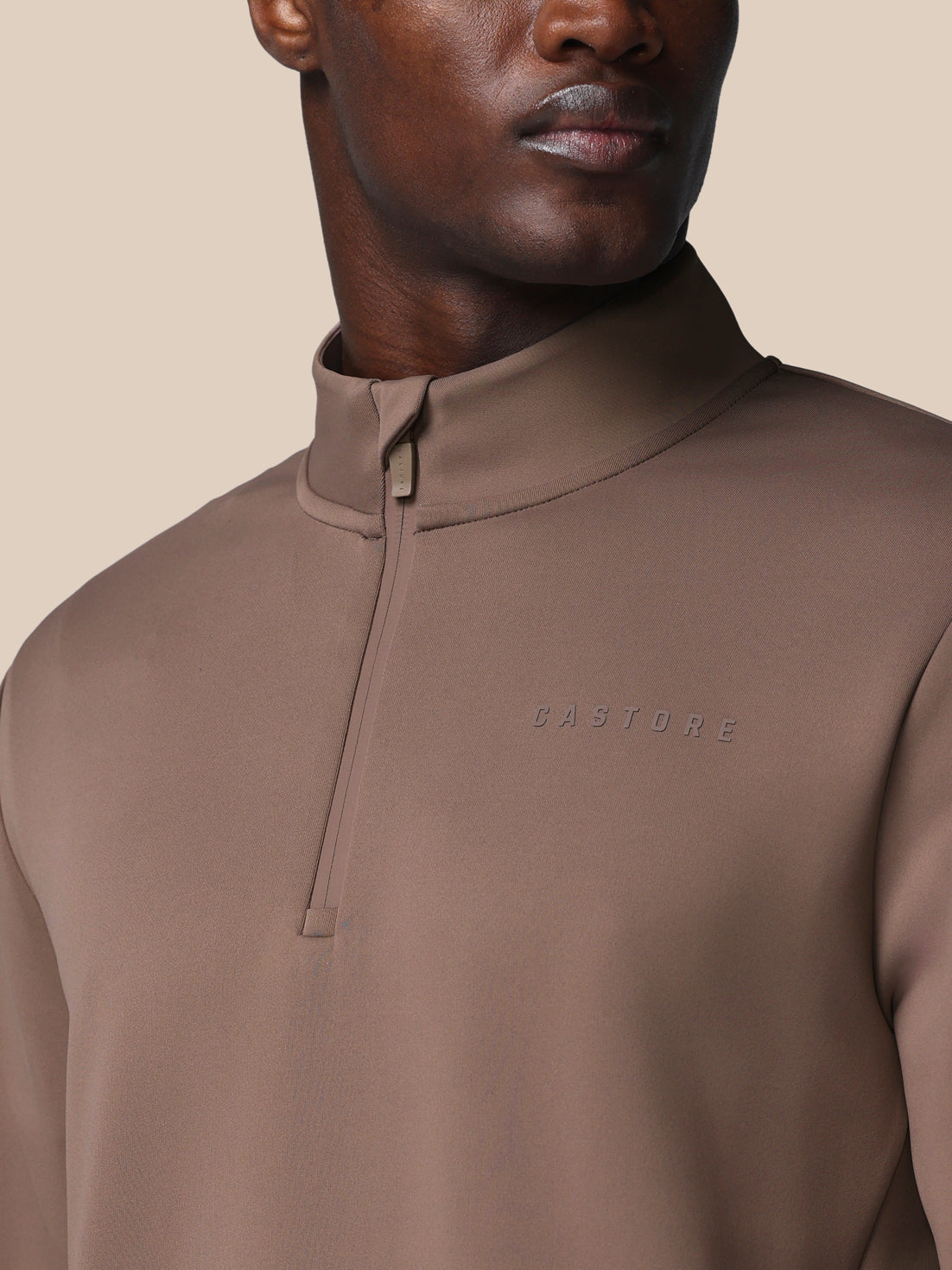 Brown quarter-zip pullover with 'Castore' branding on a beige background