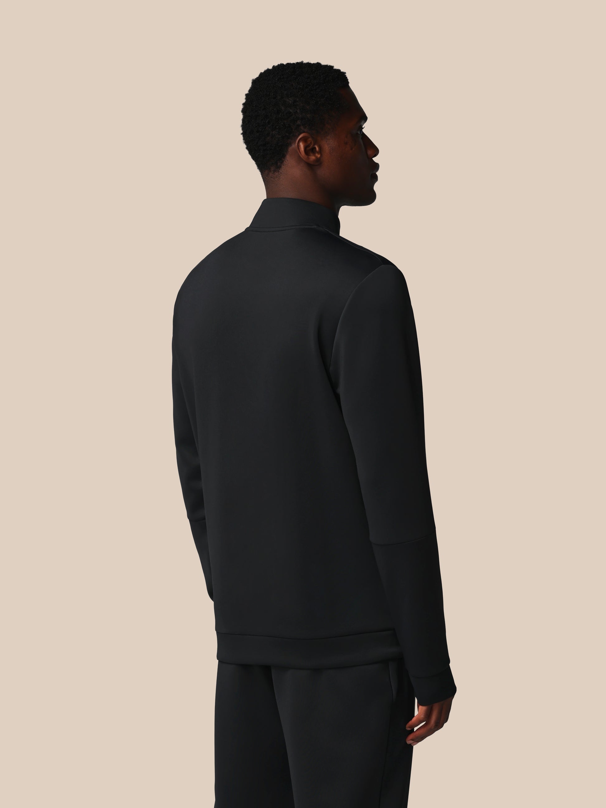 Person wearing a black quarter-zip sweatshirt and pants on a beige background