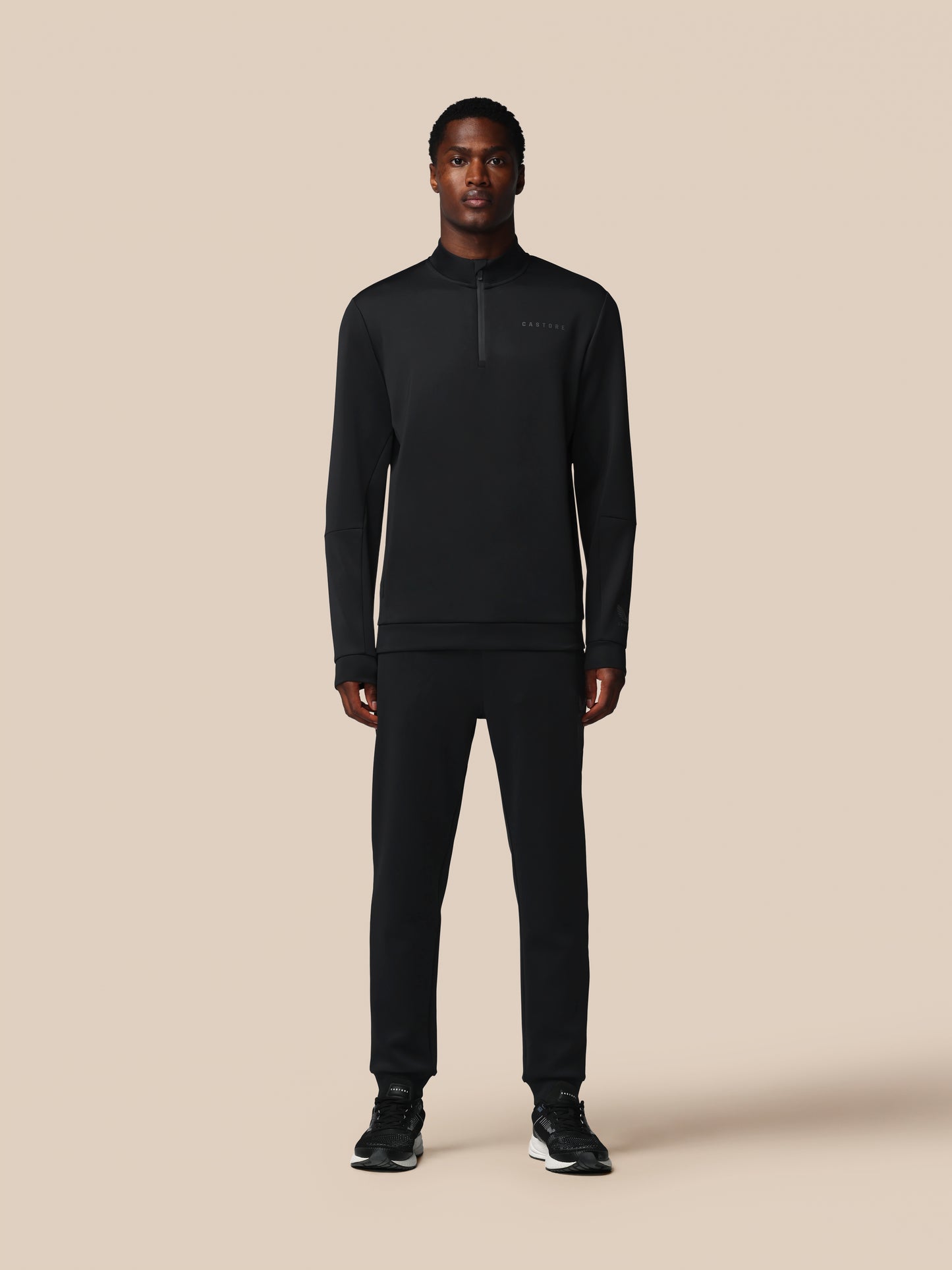 Person wearing a black half-zip sweatshirt and pants on a beige background