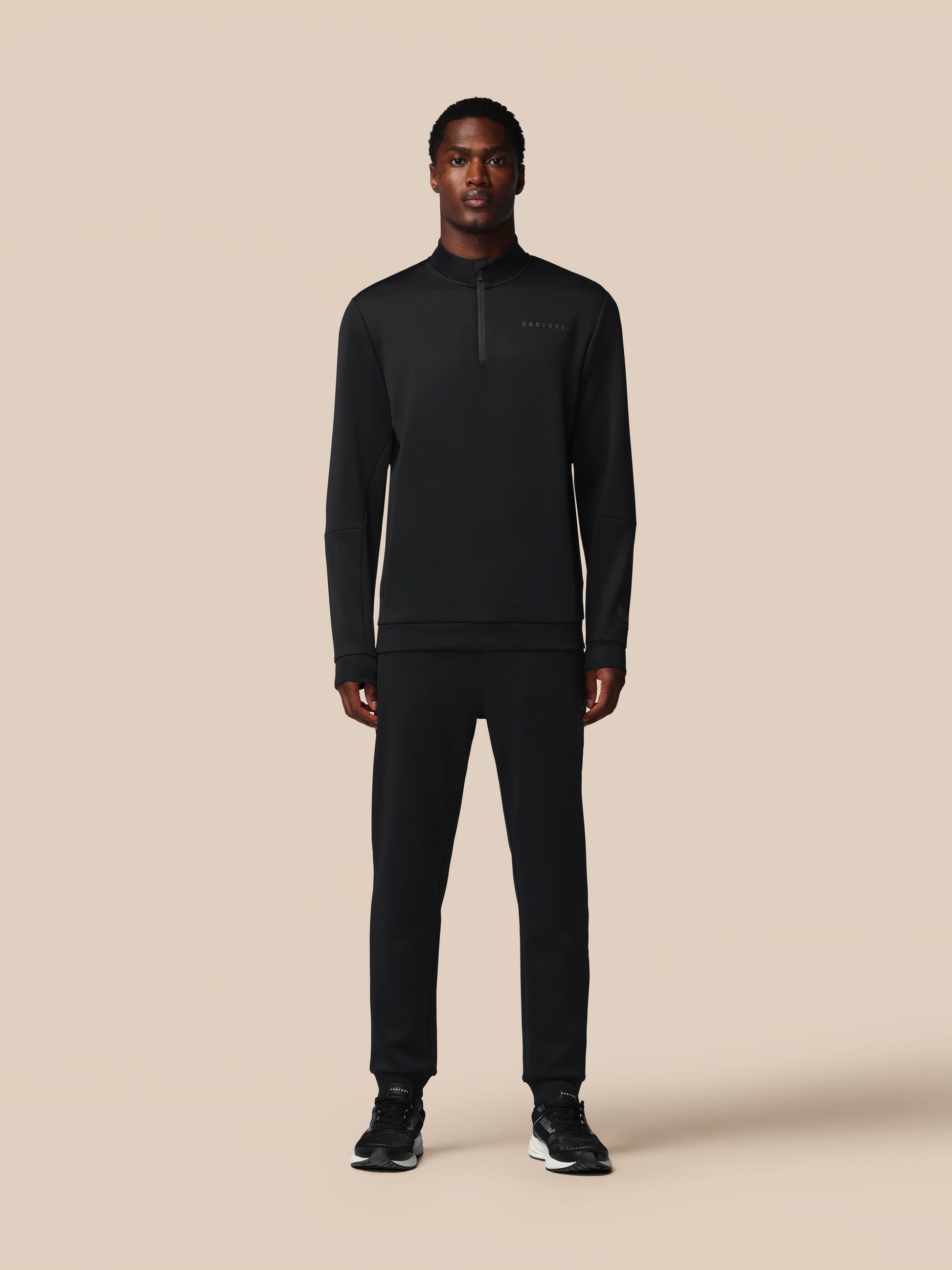 Person wearing a black half-zip sweatshirt and pants on a beige background