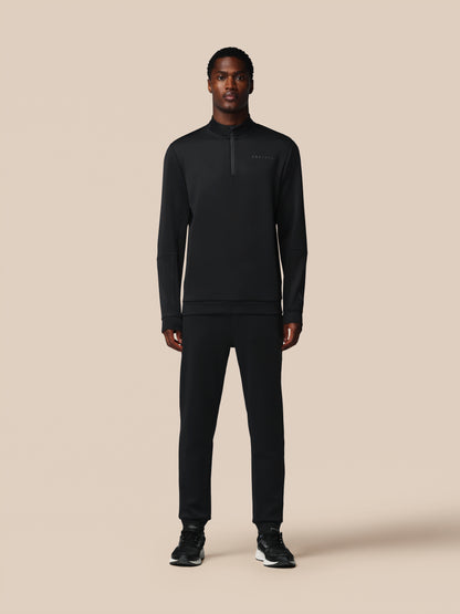 Person wearing a black half-zip sweatshirt and pants on a beige background