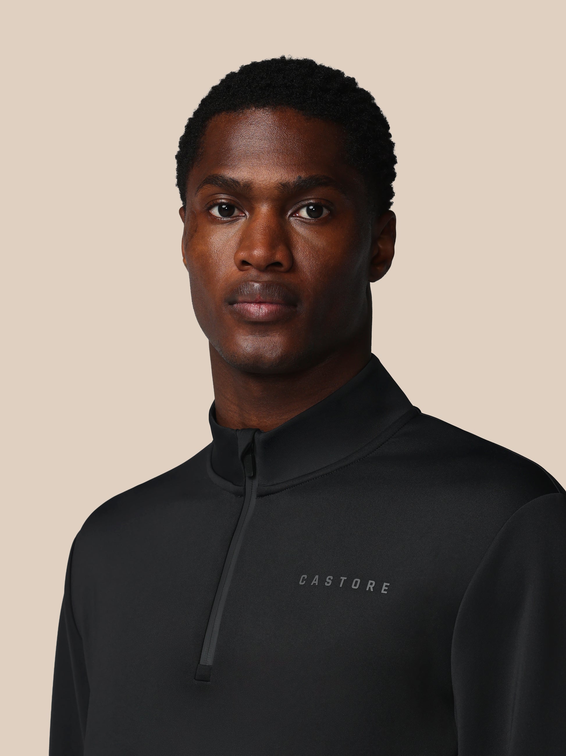 Man wearing a black jacket with 'CASTORE' branding on a beige background