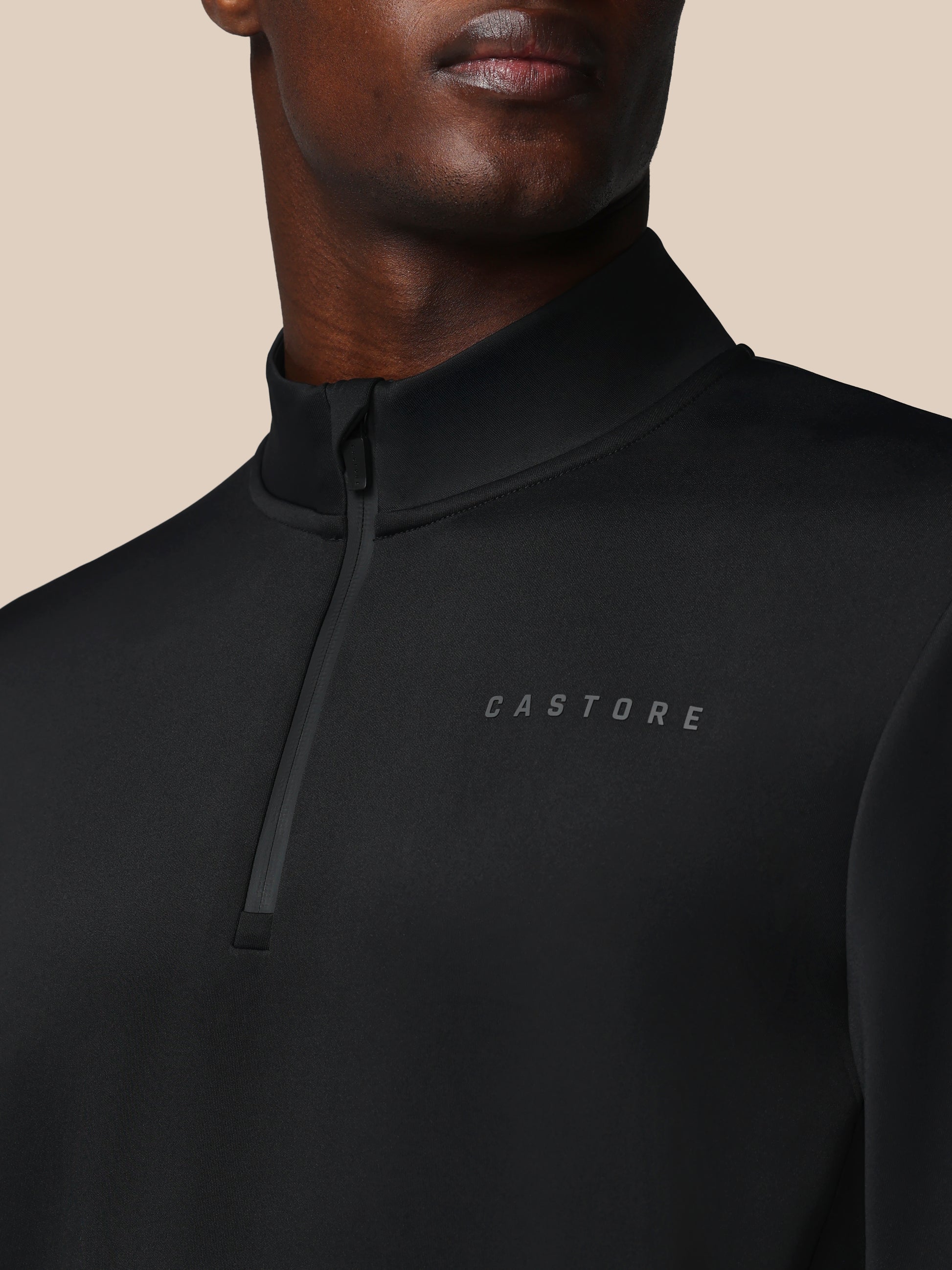 Black quarter-zip sweatshirt with 'CASTORE' logo on a beige background