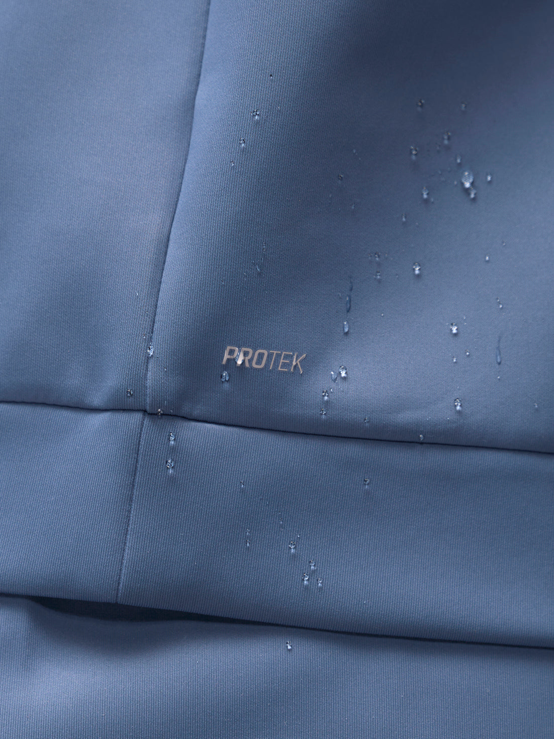 Close-up of Moonlight Blue Flex Sweatshirt fabric with PROTEK watermark and water droplets