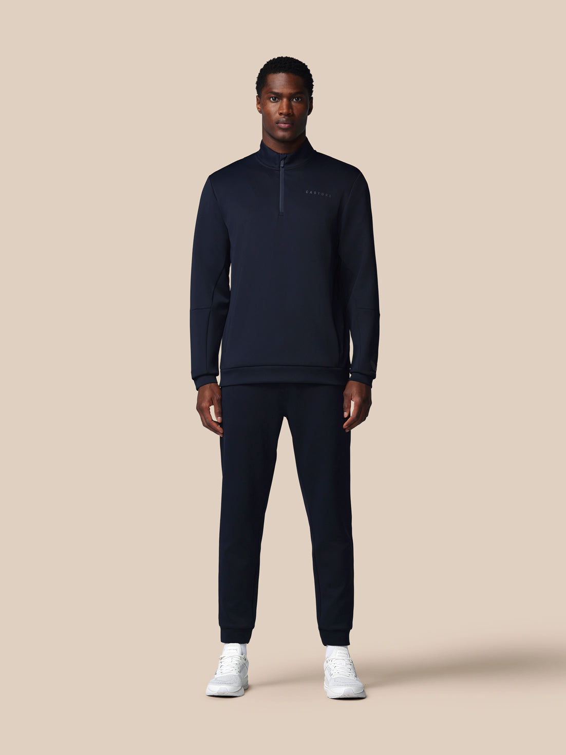 Man wearing a dark navy tracksuit on a beige background