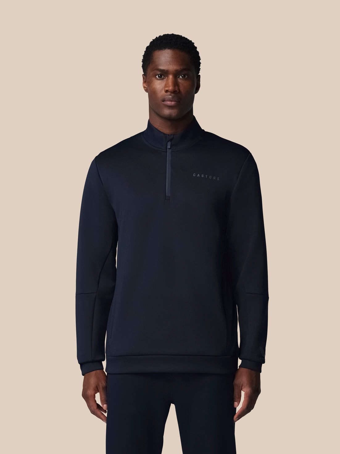Man wearing a black quarter-zip sweatshirt on a beige background