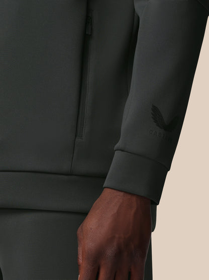 Close-up of a dark gray sweatshirt with a brand logo on the sleeve against a beige background