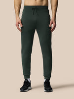 Person wearing dark green jogger pants on a beige background