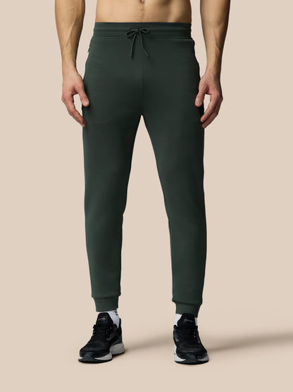 Person wearing dark green jogger pants on a beige background
