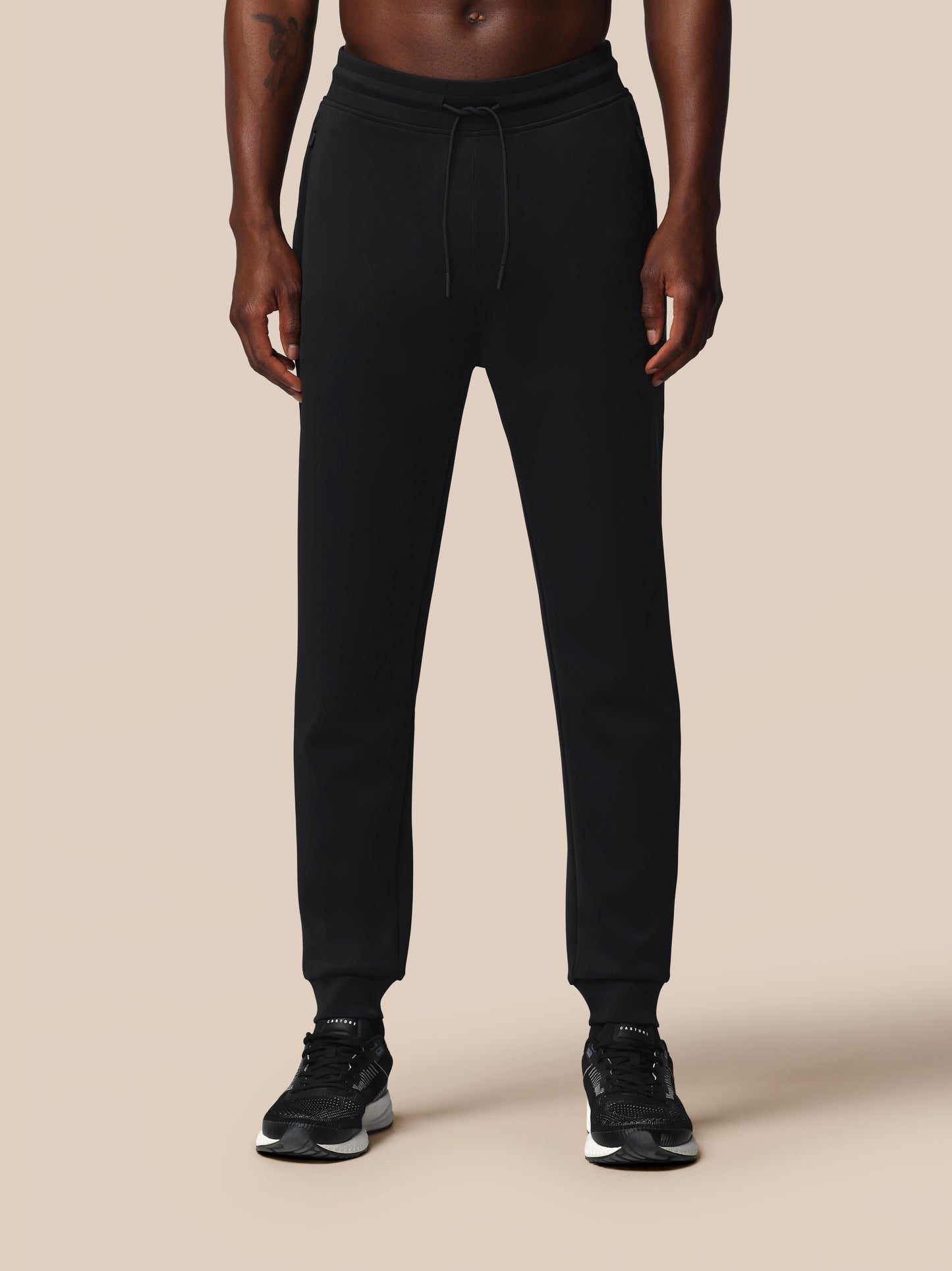 Person wearing black jogger pants on a beige background