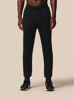 Person wearing black jogger pants on a beige background