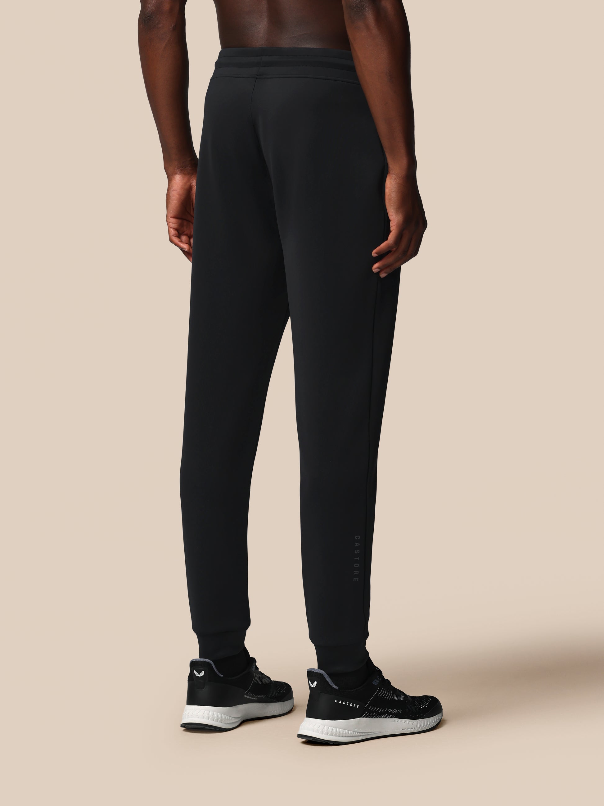 Person wearing black athletic pants and shoes on a beige background