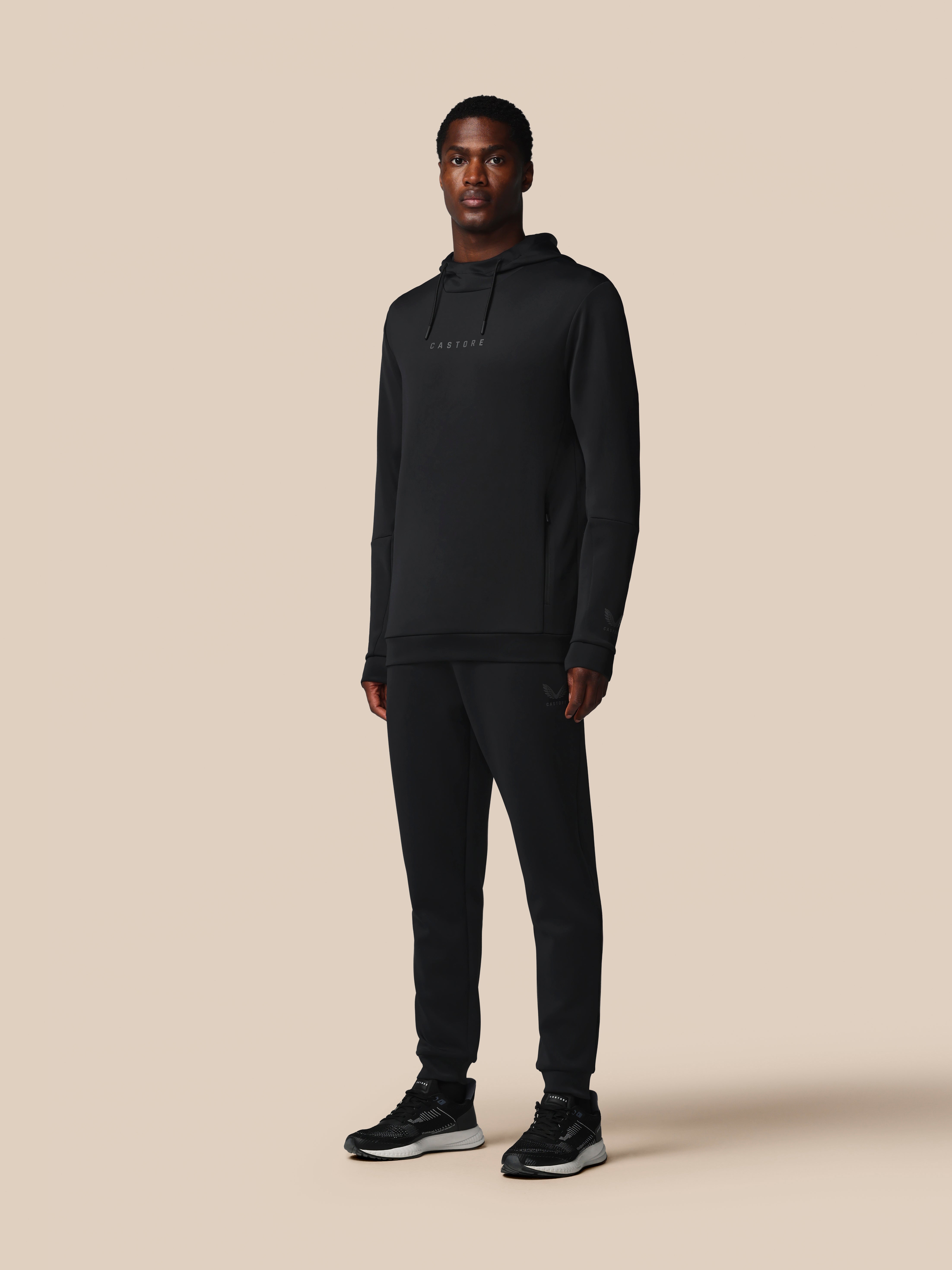 Man wearing a black hoodie and pants on a beige background