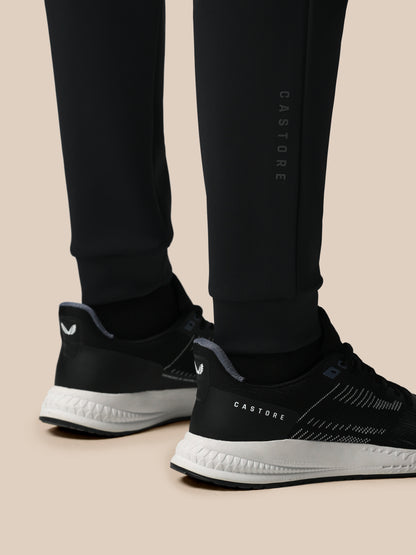 Black athletic shoes with white soles worn with black pants on a beige background