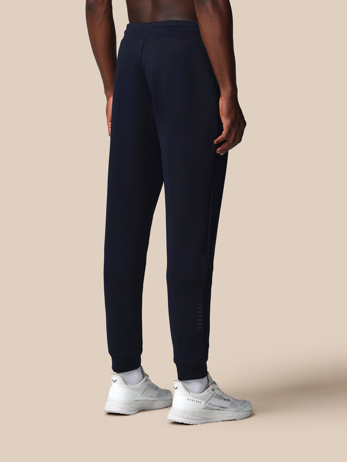 Person wearing navy blue jogger pants on a beige background