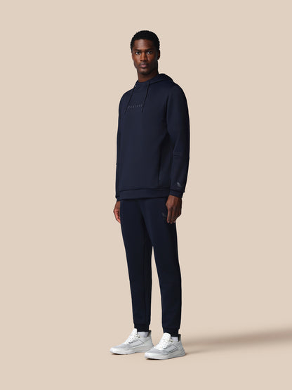 Man wearing a navy tracksuit with 'CASTORE' branding on a beige background
