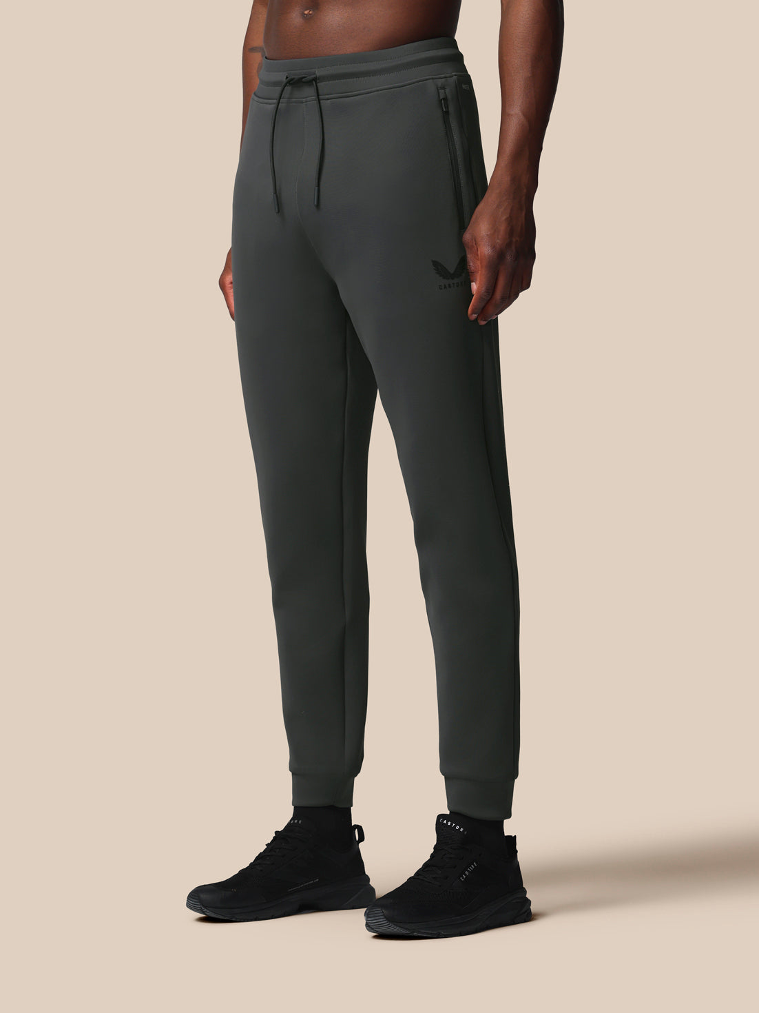 Person wearing dark gray jogger pants and black shoes on a beige background