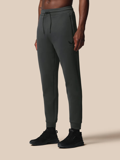 Person wearing dark gray jogger pants and black shoes on a beige background