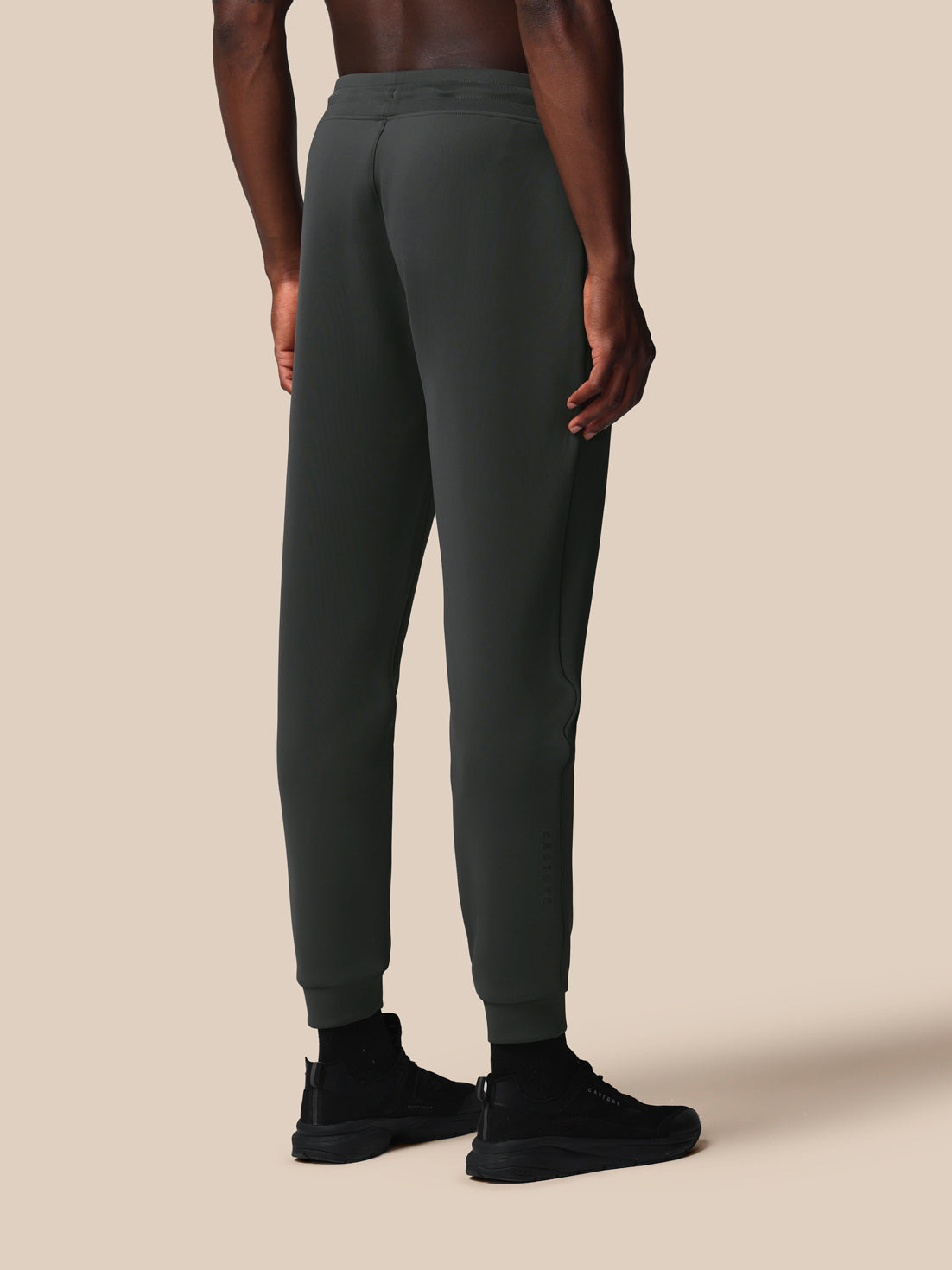 Person wearing dark gray jogger pants and black shoes on a beige background