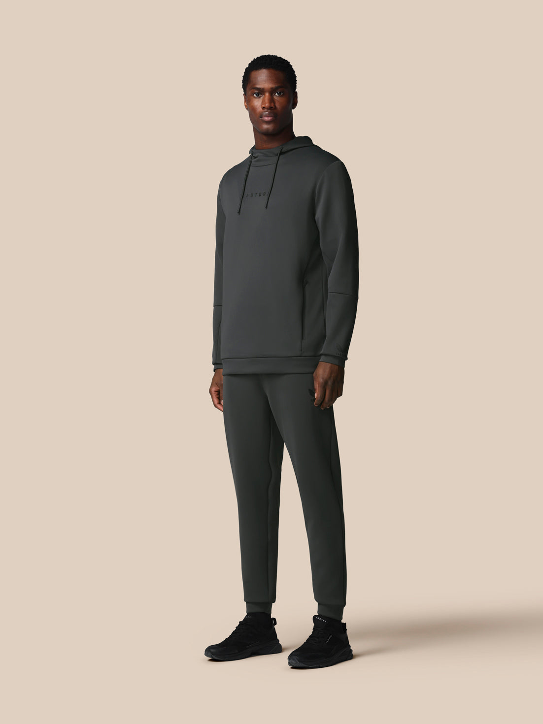 Man wearing a dark gray hoodie and pants on a beige background