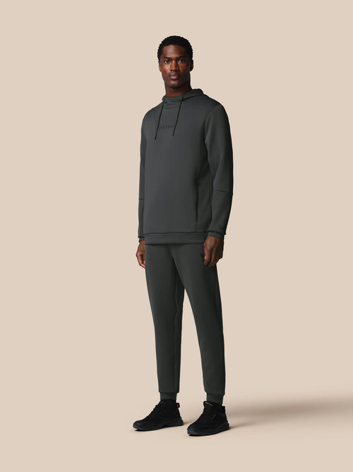 Man wearing a dark gray hoodie and pants on a beige background