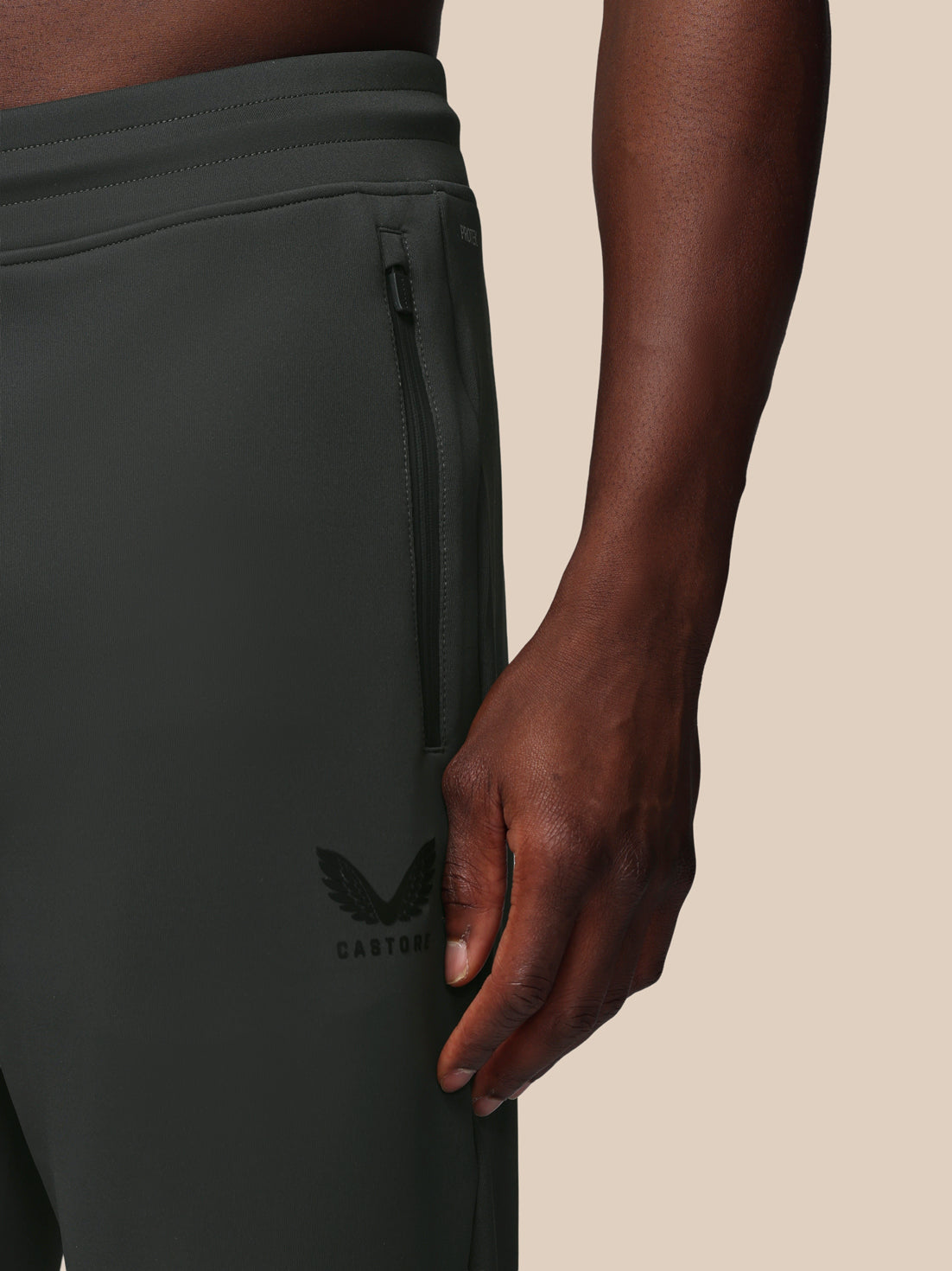 Person wearing dark gray pants with a brand logo on a beige background