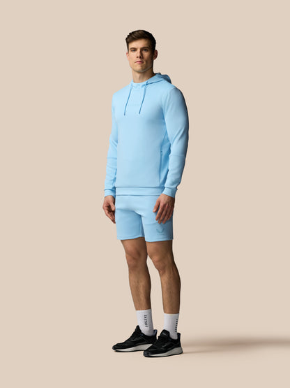 Man wearing a light blue hoodie and shorts on a beige background