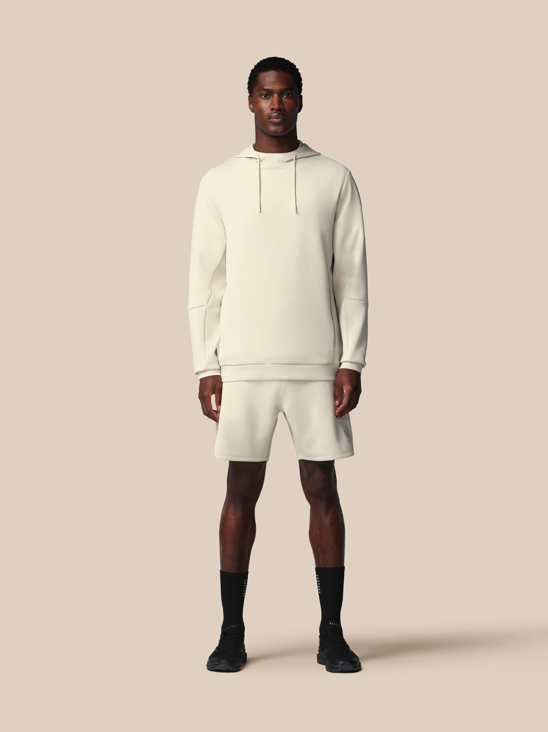 Man wearing a white hoodie and shorts set on a beige background