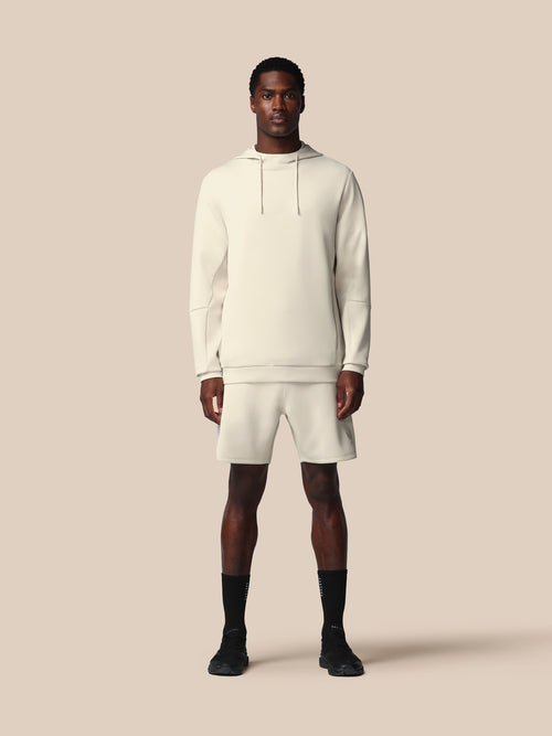 Man wearing a white hoodie and shorts set on a beige background