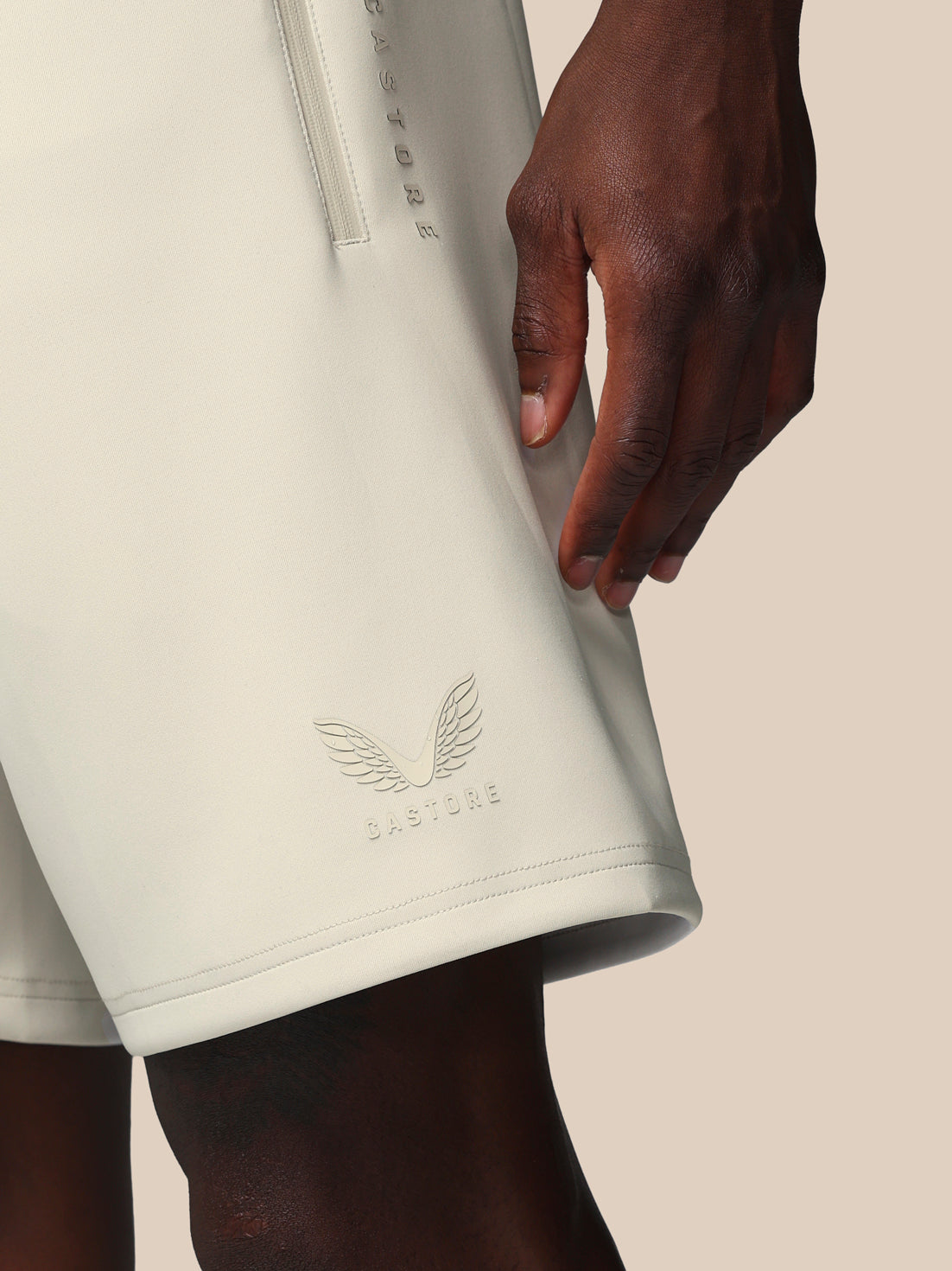 Close-up of a person wearing light-colored shorts with a brand logo on a beige background