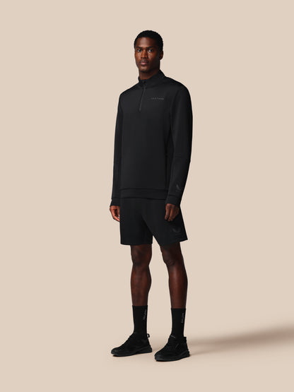 Man wearing a black pullover, shorts, and socks on a beige background
