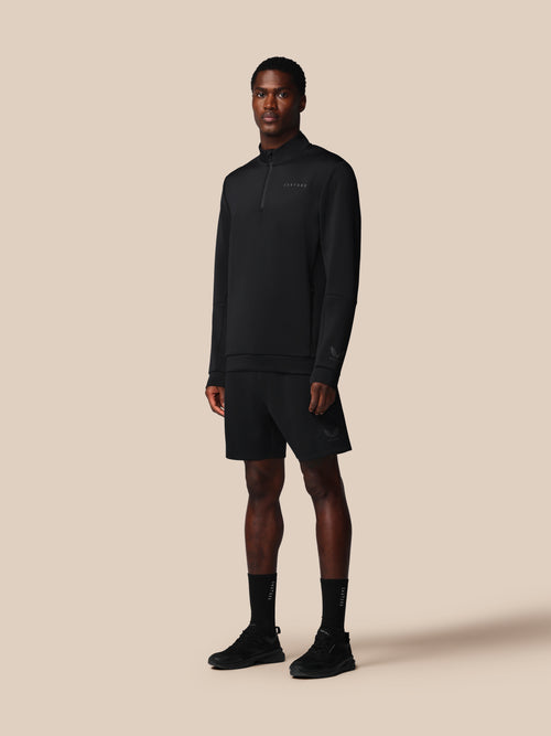 Man wearing a black pullover, shorts, and socks on a beige background