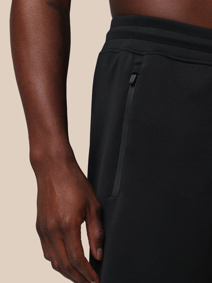 Close-up of a person wearing black pants with a beige background