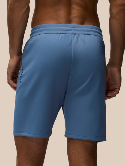 A close-up back view of a person wearing blue athletic shorts against a plain beige studio background.