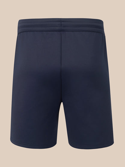A pair of dark navy athletic shorts shown from the back, featuring a wide elastic waistband, on a solid beige background.
