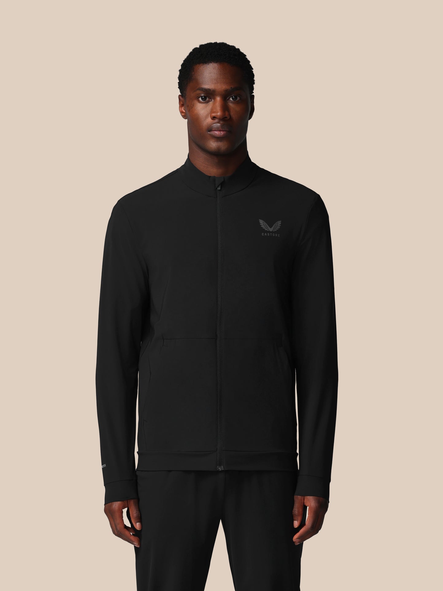 Man wearing a black jacket with a logo on a beige background