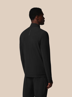 Person wearing a black half-zip pullover and pants on a beige background