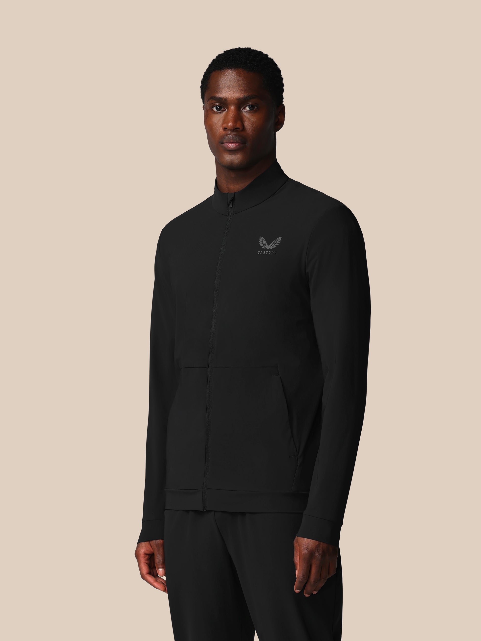 Man wearing a black jacket with a logo on a beige background
